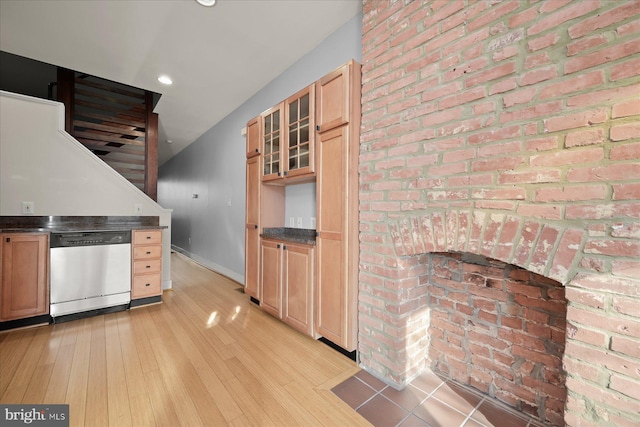 kitchen with stainless steel dishwasher, light hardwood / wood-style floors, brick wall, and light brown cabinetry