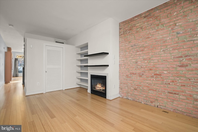 unfurnished living room with light wood-type flooring and brick wall