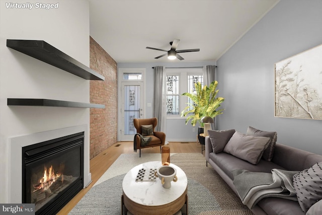 living room featuring ornamental molding, brick wall, ceiling fan, light hardwood / wood-style flooring, and a fireplace