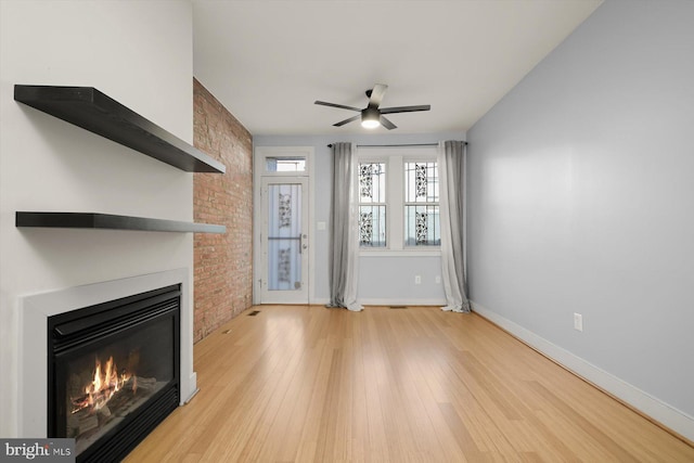 unfurnished living room with ceiling fan, brick wall, and light wood-type flooring