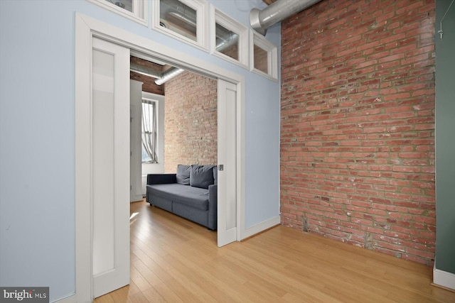 hallway featuring light wood-type flooring and brick wall