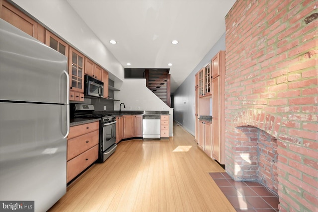 kitchen with appliances with stainless steel finishes, sink, light hardwood / wood-style floors, and brick wall