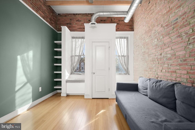 unfurnished living room featuring beamed ceiling, brick wall, a high ceiling, and light wood-type flooring