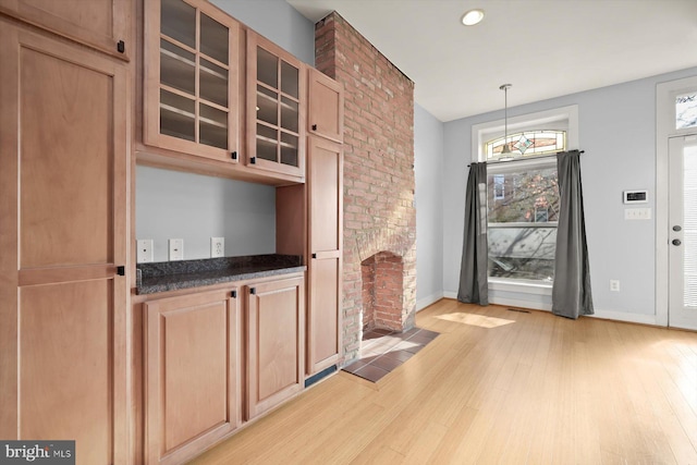 interior space featuring a brick fireplace, dark stone countertops, decorative light fixtures, and light wood-type flooring