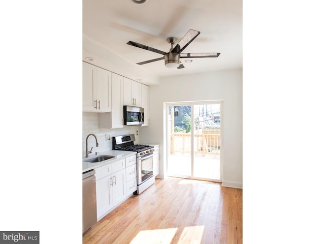 kitchen featuring decorative backsplash, stainless steel appliances, sink, white cabinets, and light hardwood / wood-style floors