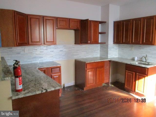 kitchen featuring light stone countertops, tasteful backsplash, dark wood-type flooring, and sink