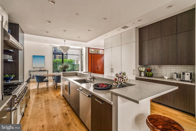 kitchen featuring decorative light fixtures, a sink, backsplash, and light wood finished floors