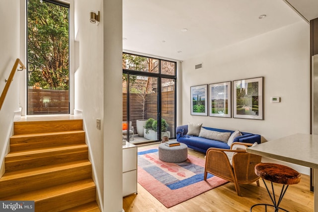 living room featuring expansive windows, visible vents, stairway, and light wood finished floors