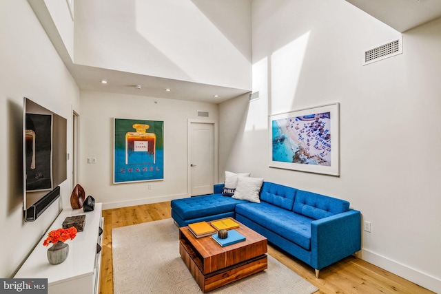 living area with a towering ceiling, visible vents, and wood finished floors