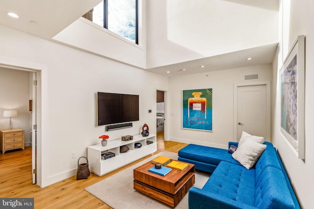 living area featuring baseboards, visible vents, a towering ceiling, wood finished floors, and recessed lighting