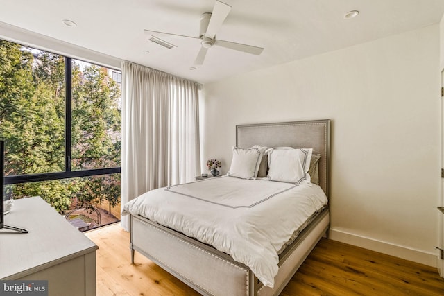 bedroom with a ceiling fan, visible vents, baseboards, and wood finished floors