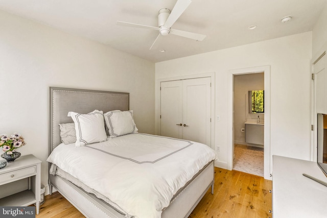 bedroom with baseboards, ensuite bath, light wood-style flooring, ceiling fan, and a closet