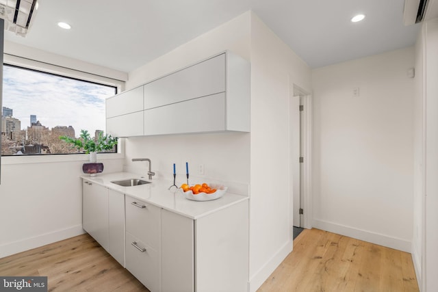 kitchen featuring a city view, a sink, white cabinetry, light countertops, and light wood finished floors