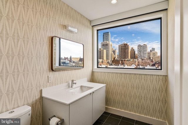 half bathroom featuring wallpapered walls, toilet, tile patterned floors, a view of city, and vanity