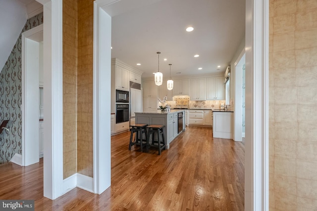 kitchen featuring a kitchen breakfast bar, black appliances, decorative light fixtures, hardwood / wood-style floors, and an island with sink