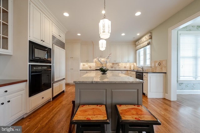 kitchen featuring a center island, light stone counters, light hardwood / wood-style flooring, pendant lighting, and black appliances