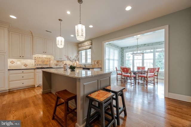 kitchen featuring dark stone counters, light wood-type flooring, decorative light fixtures, a kitchen island, and a kitchen bar