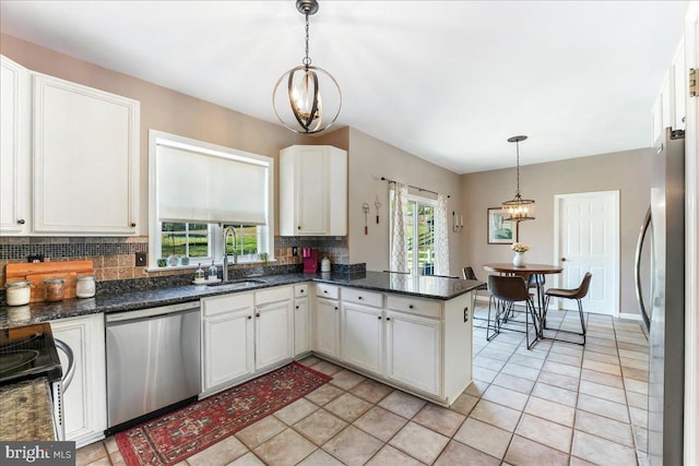 kitchen featuring backsplash, stainless steel appliances, sink, white cabinets, and hanging light fixtures