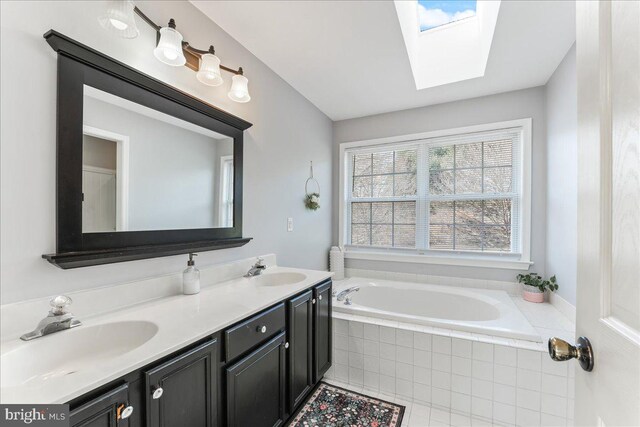 bathroom with a skylight, tile patterned flooring, vanity, and a relaxing tiled tub