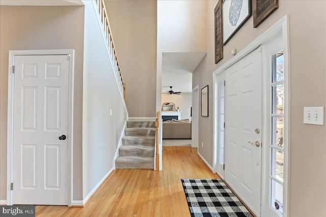 foyer entrance featuring ceiling fan, a towering ceiling, and light hardwood / wood-style flooring