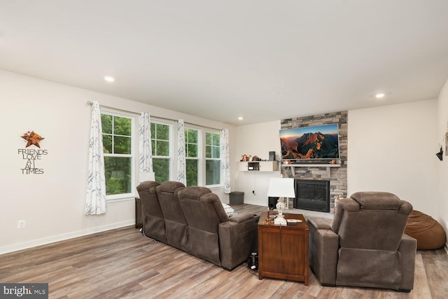 living area featuring light wood finished floors, a stone fireplace, recessed lighting, and baseboards