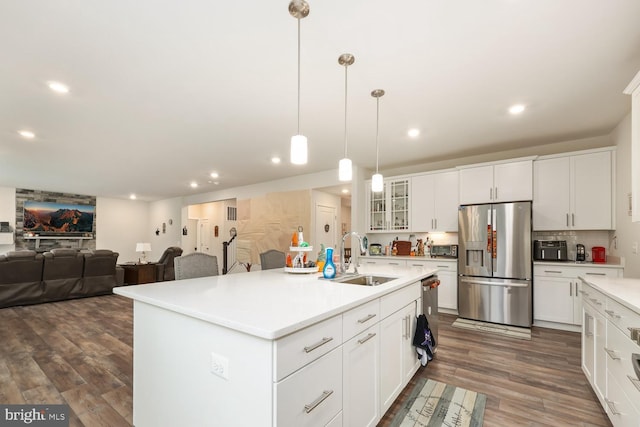 kitchen featuring a sink, light countertops, an island with sink, stainless steel fridge, and glass insert cabinets