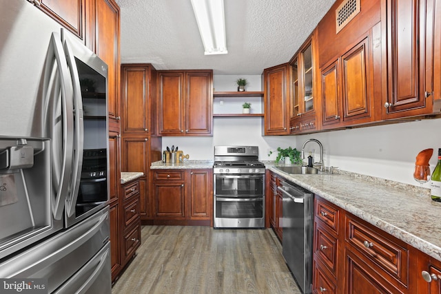 kitchen featuring sink, a textured ceiling, appliances with stainless steel finishes, dark hardwood / wood-style flooring, and light stone counters