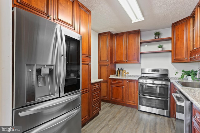 kitchen featuring light stone countertops, appliances with stainless steel finishes, a textured ceiling, and light hardwood / wood-style floors