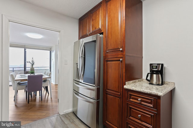 kitchen featuring light stone countertops, stainless steel refrigerator with ice dispenser, light wood-type flooring, and a textured ceiling