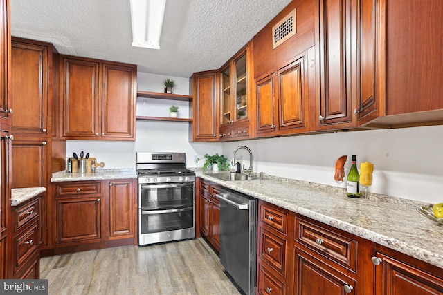 kitchen with sink, light wood-type flooring, a textured ceiling, light stone counters, and stainless steel appliances