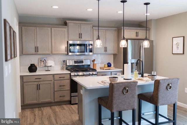 kitchen featuring backsplash, a center island with sink, decorative light fixtures, and appliances with stainless steel finishes