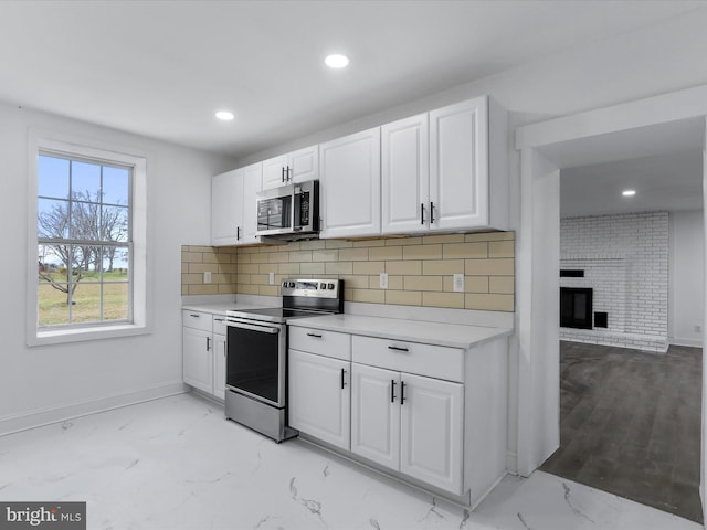 kitchen with white cabinets, backsplash, appliances with stainless steel finishes, and a brick fireplace