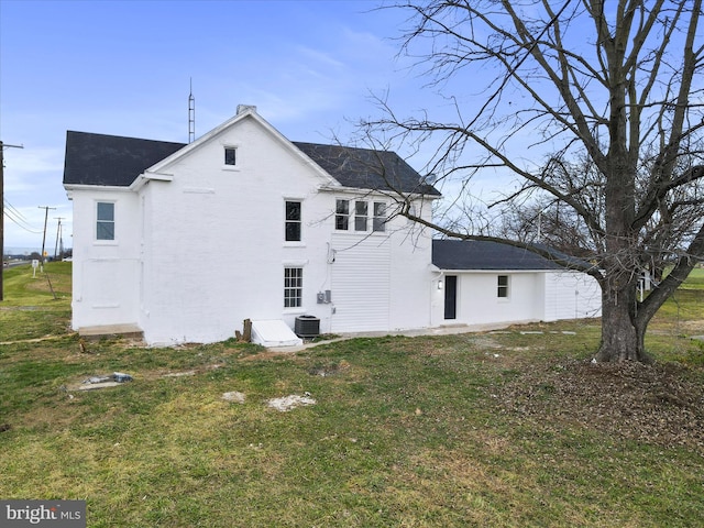 rear view of house featuring central AC unit and a lawn