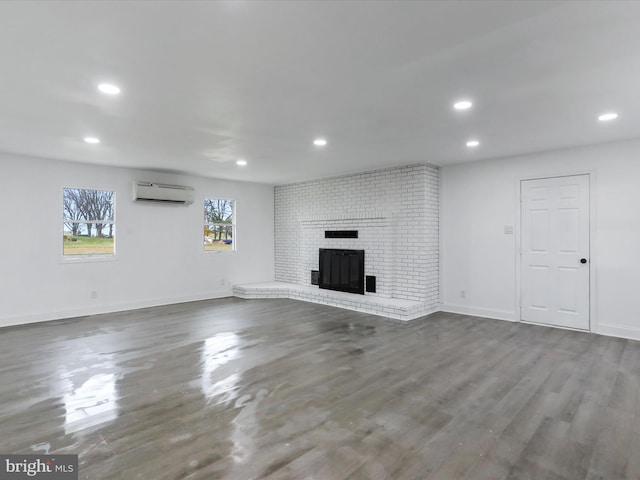 unfurnished living room featuring a wall mounted air conditioner, hardwood / wood-style flooring, and a brick fireplace