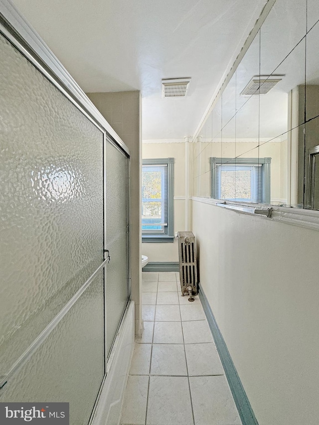 bathroom with tile patterned floors, combined bath / shower with glass door, toilet, ornamental molding, and radiator heating unit