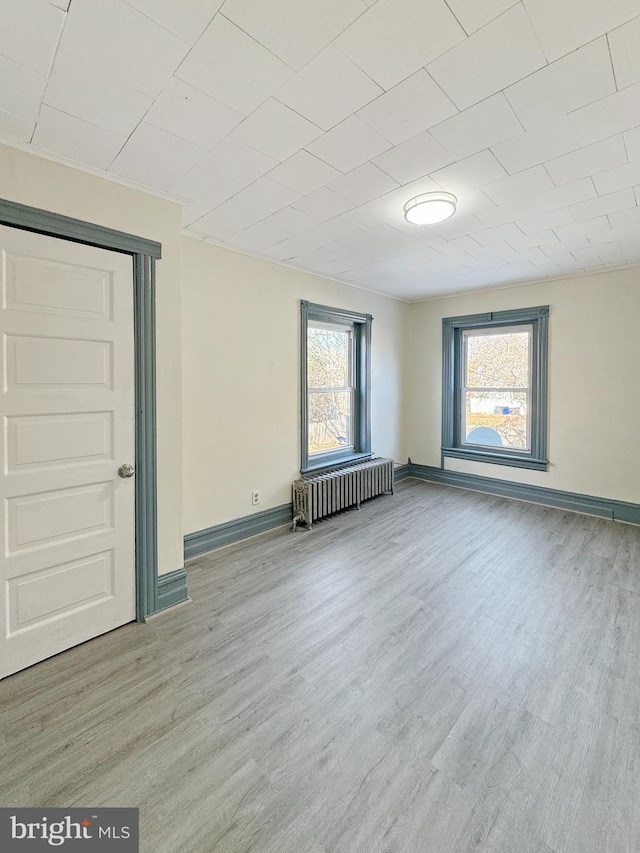 empty room with light hardwood / wood-style flooring, radiator, and a healthy amount of sunlight