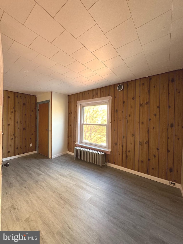 spare room featuring radiator, wood walls, and wood-type flooring