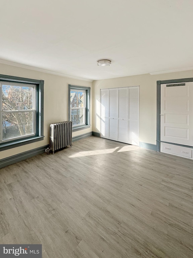 unfurnished bedroom featuring radiator heating unit, crown molding, and light hardwood / wood-style flooring