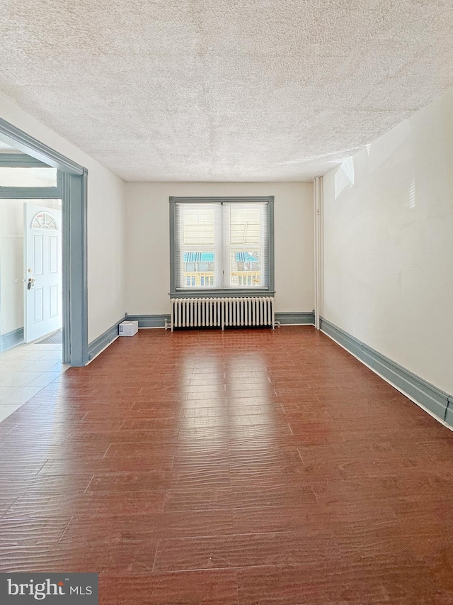 spare room with radiator heating unit, a textured ceiling, and dark wood-type flooring