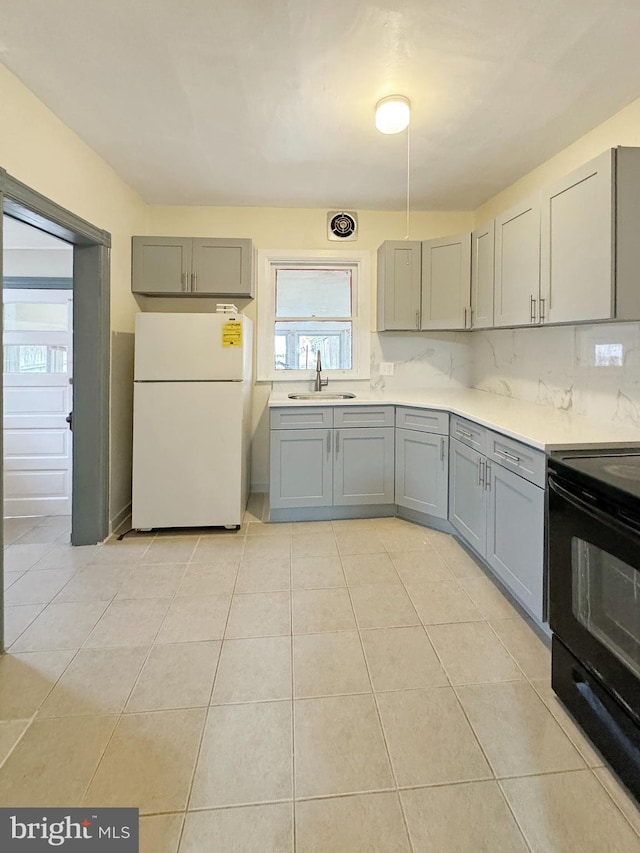 kitchen featuring backsplash, gray cabinetry, sink, white refrigerator, and black electric range