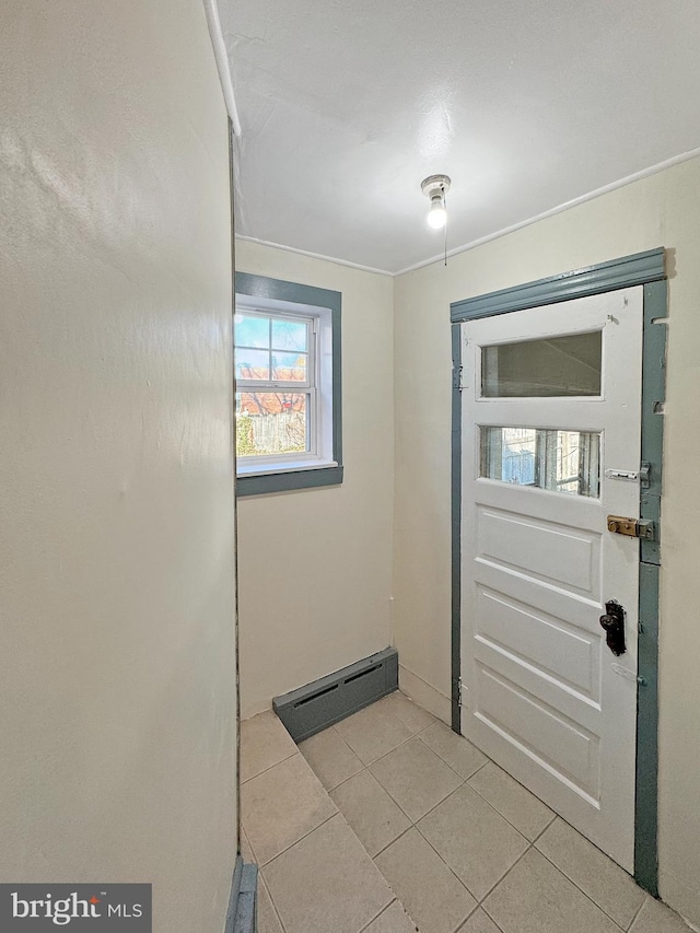 doorway with crown molding, light tile patterned flooring, and a baseboard heating unit