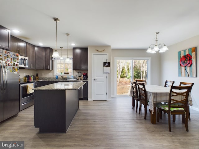 kitchen with appliances with stainless steel finishes, light wood-type flooring, light stone counters, decorative light fixtures, and a kitchen island