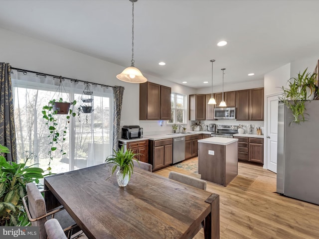 kitchen featuring sink, a center island, stainless steel appliances, pendant lighting, and light wood-type flooring