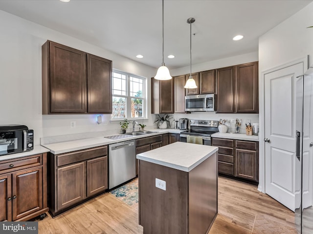 kitchen with light hardwood / wood-style flooring, a kitchen island, pendant lighting, and appliances with stainless steel finishes