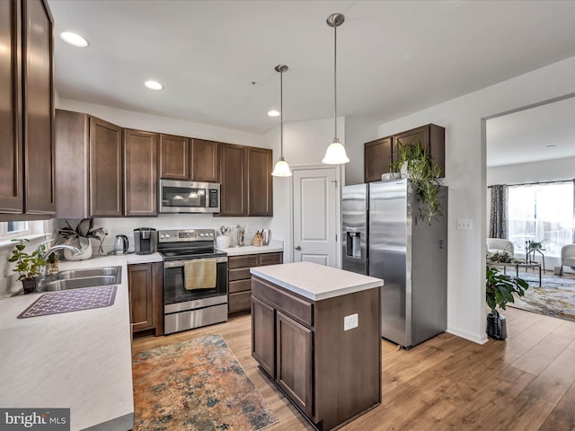 kitchen with stainless steel appliances, sink, decorative light fixtures, light hardwood / wood-style flooring, and a center island