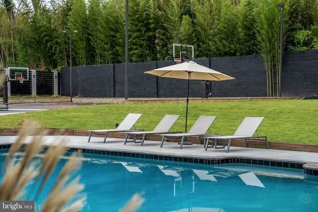 view of swimming pool with basketball hoop and a yard