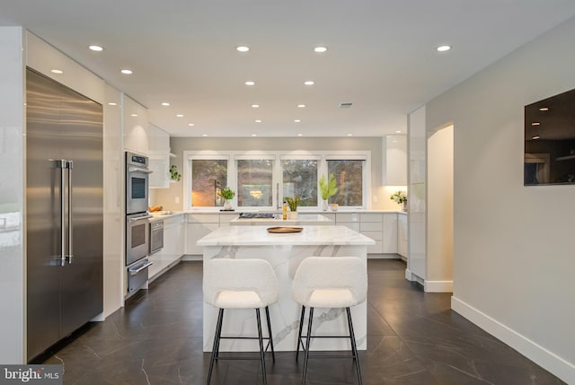 kitchen with white cabinetry, a center island, light stone countertops, a breakfast bar, and appliances with stainless steel finishes