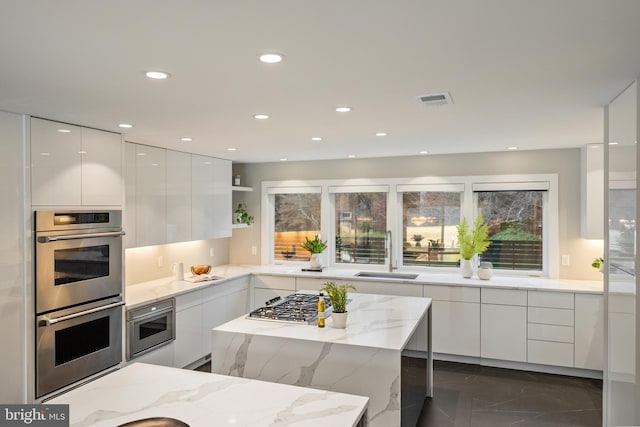 kitchen featuring light stone counters, stainless steel appliances, white cabinetry, and sink