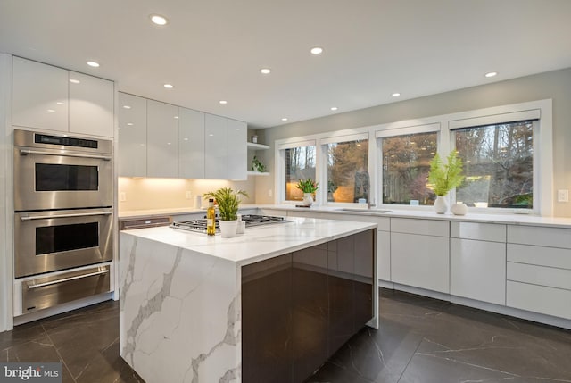 kitchen with a center island, white cabinets, sink, light stone countertops, and stainless steel appliances