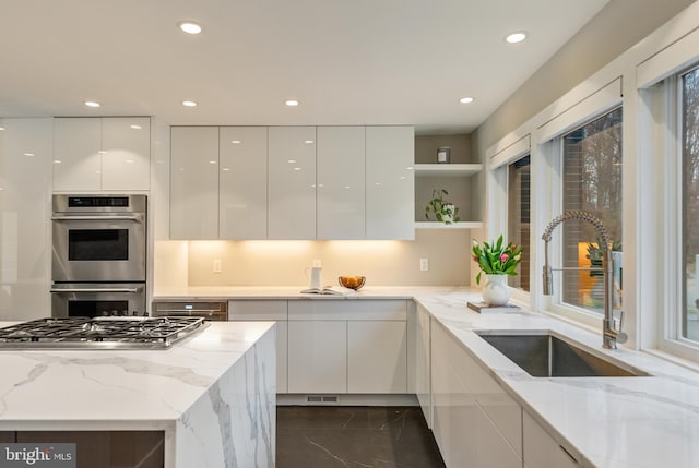 kitchen with appliances with stainless steel finishes, white cabinetry, light stone counters, and sink